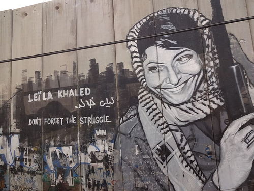 Click photo to download. Caption: The Israeli security fence in Bethlehem is pictured here painted with graffiti depicting Popular Front for the Liberation of Palestine terrorist Leila Khaled. Rabab Abdulhadi, a professor at San Francisco State University, met with Khaled on a trip funded by the state of California. Credit: Bluewind via Wikimedia Commons.