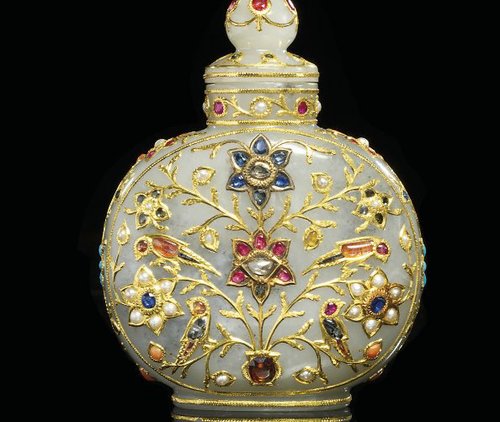 A Mughal-style gemstone-encrusted white jade scent bottle. 18th/19th century. Of flattened circular shape on a short oval foot, the cylindrical neck fitted with a screw-top cover with a knop finial, the body inlaid in gold and inset with gem stones including diamonds, rubies, sapphires and emeralds, depicting two panels on the front and back enclosing birds and blossoming branches, the sides with further blossoms.