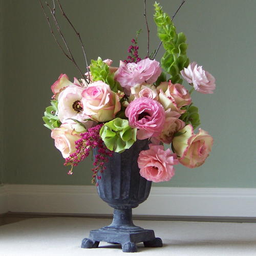 Romantic garden style arrangement with bells of Ireland, Cezanne roses, pink ranunculus, heather and birch branches in a cast iron urn.