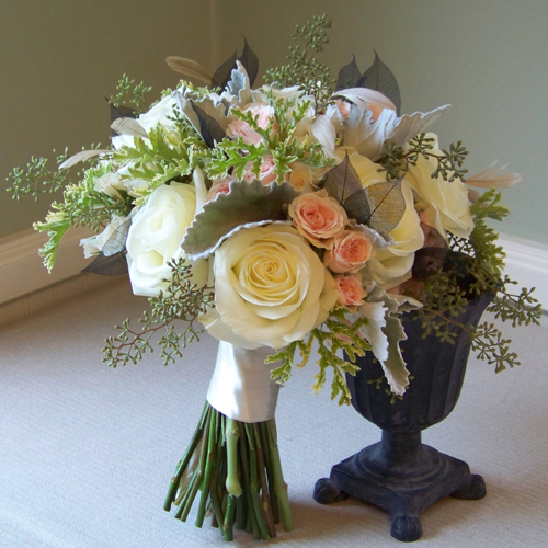 bridal bouquet containing black skeleton leaves, beige stripped coque feathers, Polar Star roses, Princess spray roses, Peach Vision spray roses, scented geranium, seeded eucalyptus, and dusty miller