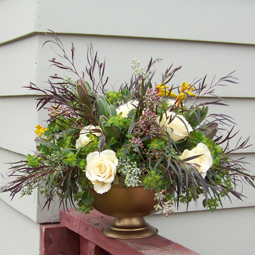 centerpiece with yellow kangaroo paws, Cream Prophyta roses, green leucadendron, agonis, bupleurum, and seeded eucalyptus in a gold footed bowl