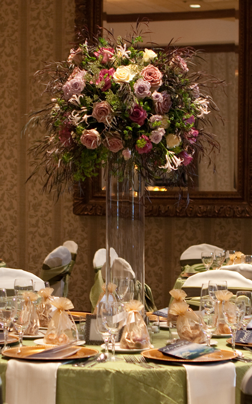tall centerpiece with Amnesia roses, Maritim roses, Cream Prophyta roses, Little Silver spray roses, blush nerine lilies, agonis, bupleurum, and seeded eucalyptus on a 32 inch cylinder vase
