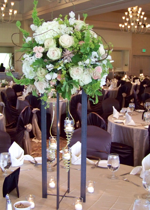 tall centerpiece with white sweet peas, white hydrangea, Green Fashion roses, blush astilbe, Star Blush spray roses, alchemilla, bupleurum, bells of Ireland, scented geranium, and curly willow.  An iron stand and spiraled hanging votive holders complete the look.
