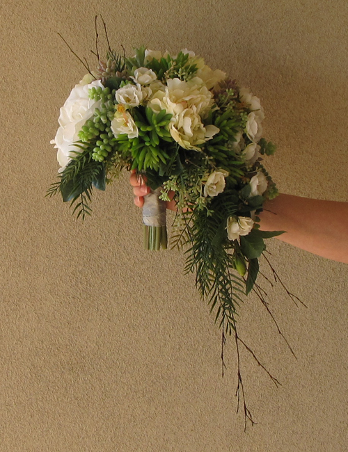 asymmetrical, crescent, cascade bridal bouquet made up of silk gardenias, white garden roses, ivory peonies, sedum, donkey tail, seeded eucalyptus, ferns, and bamboo branches.