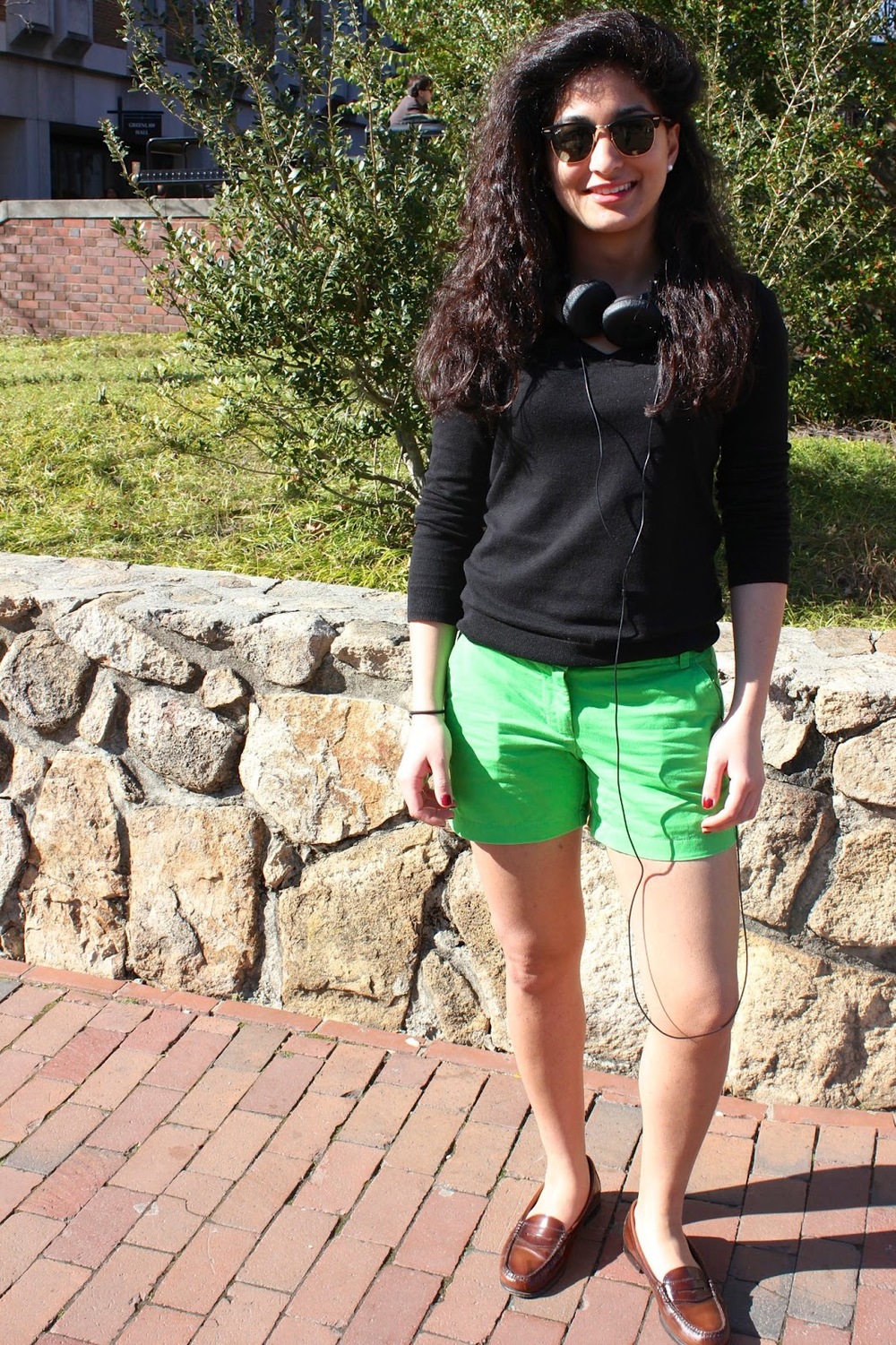 Nayab a UNC Chapel Hill student wears a simple long-sleeved black sweater over pair of lime green shorts and a pair of brown preppy penny loafers on campus.