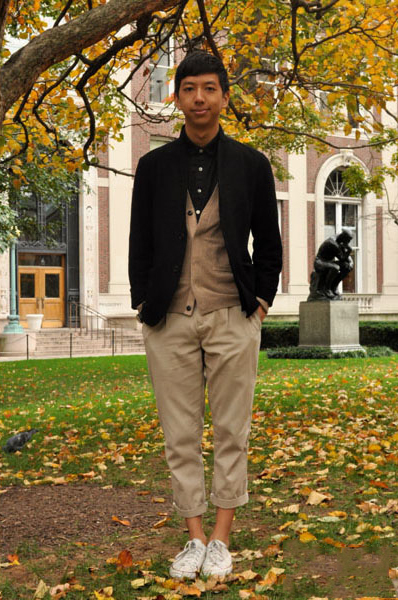 Columbia University Ethan Wong wears a neutral black and tan collegiate preppy outfit: black blazer, tan cardigan over a black shirt paired with cropped rolled-up tan chinos and white converse sneakers.